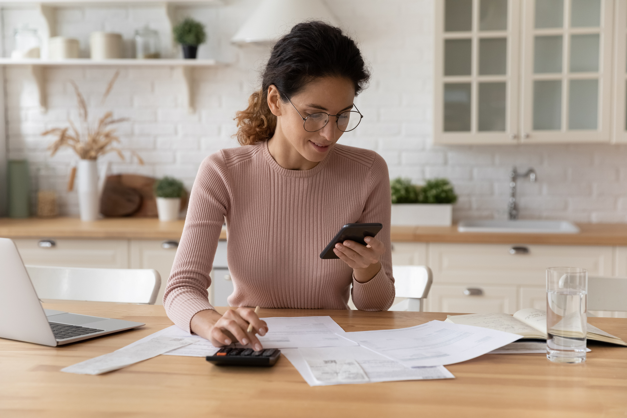 Woman reviewing household bills and calculating house cleaning costs at her kitchen table.”