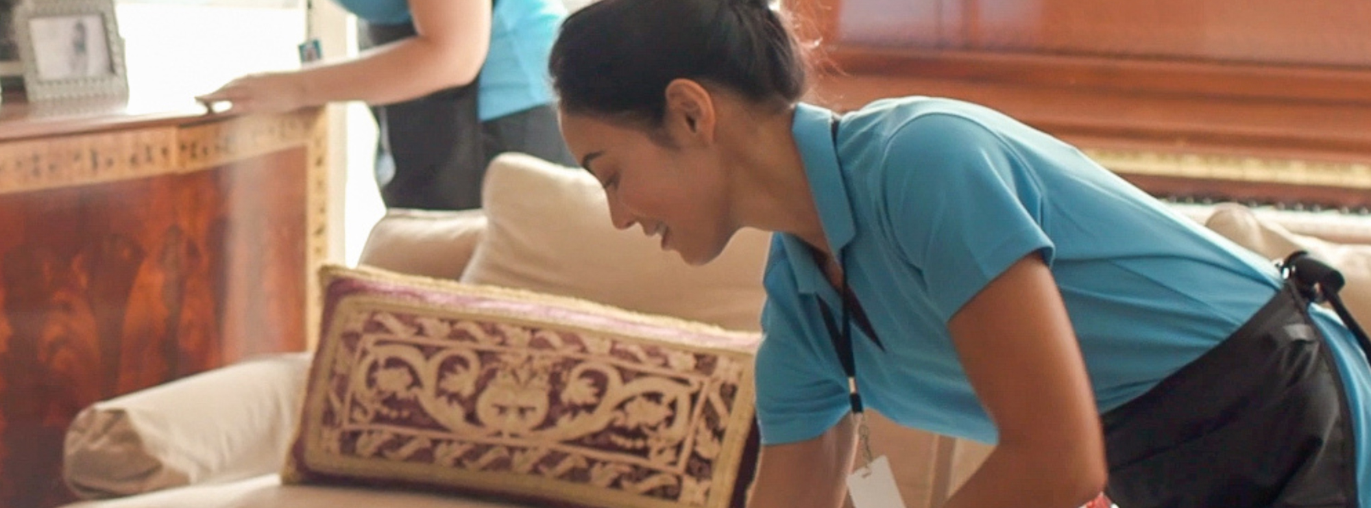 Cleaner wiping furniture during a detailed deep cleaning, reaching under surfaces for thorough dust removal.